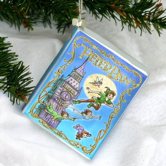 A miniature glass book-shaped Christmas tree decoration featuring illustrations of characters from the story 'Peter Pan', with gold hanging wire.