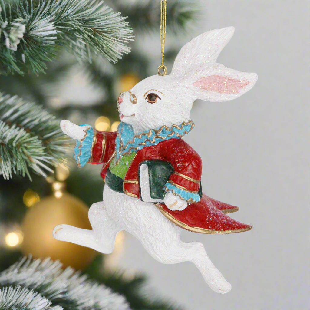 A glittery white rabbit hanging as a Christmas tree decoration, dressed in a red coat with tails, carrying a book, and wearing a crown.