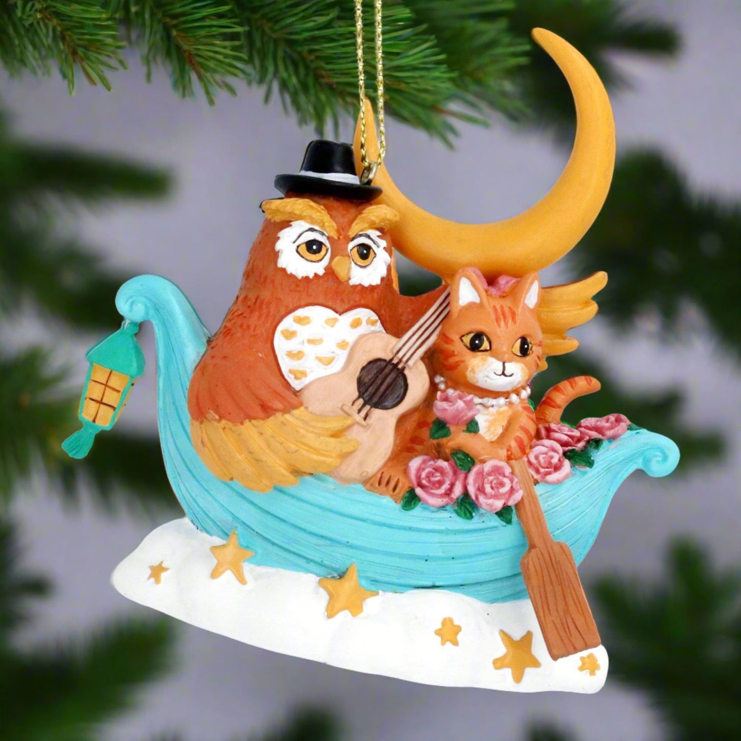 A decorative Christmas tree ornament featuring an owl and a pussycat in a boat, with a gold hanging wire and resin construction.