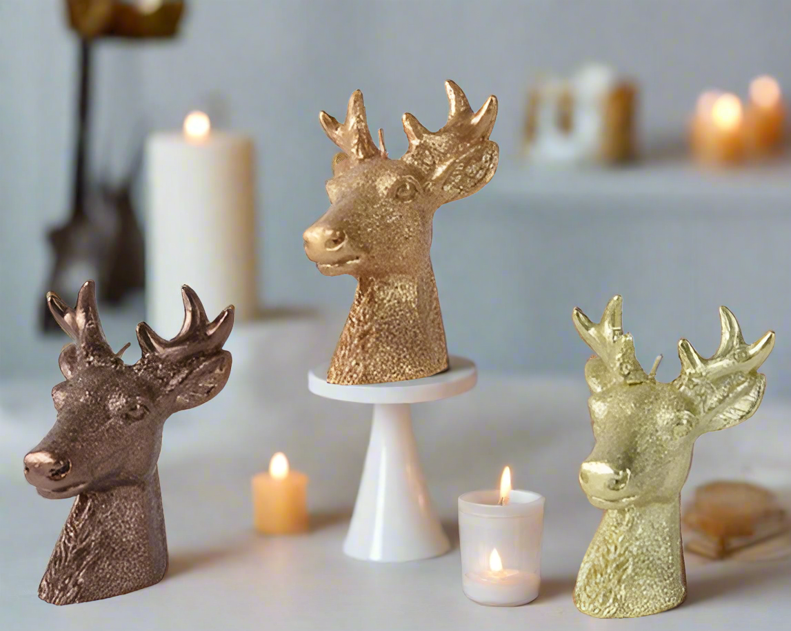 Decorative deer heads in bronze, gold, and silver on a white surface with candles.