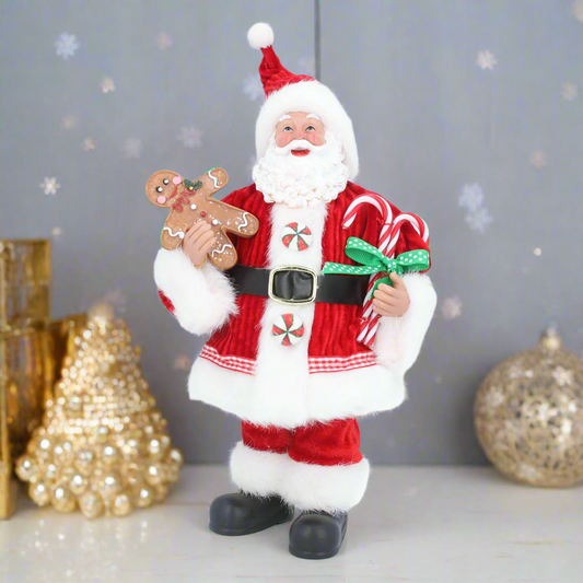 A Candy Cane Santa figure holding a gingerbread man and candy canes, dressed in a red suit with white trim and a white beard, standing against a background of Christmas decorations.