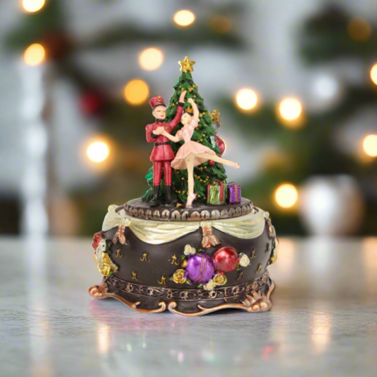 A music box featuring a nutcracker and a ballet dancer performing on a revolving base, decorated with Christmas-themed ornaments.