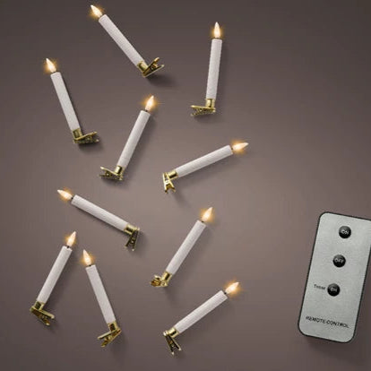 White candles with gold bases arranged on a brown surface next to a remote control.