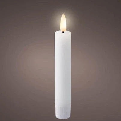 A single white flat top wax dinner candle with an LED wick, emitting a warm white glow, placed on a textured surface.