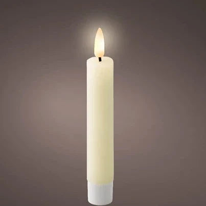 A single white flat top wax dinner candle with an LED wick, emitting a soft warm white glow, placed on a dark background.