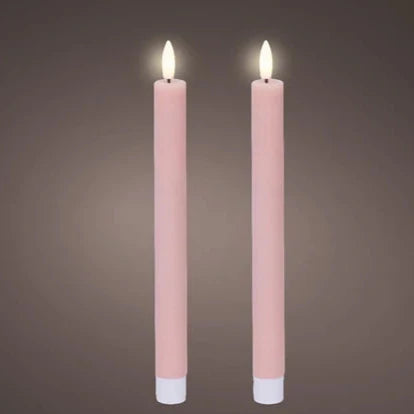A pair of light pink, flat top LED wax dinner candles with a warm white glow, standing upright against a grey background.