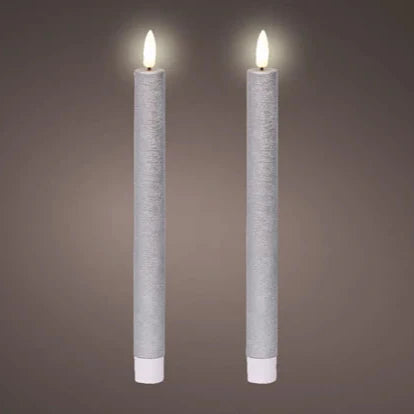 A set of two silver flat top LED wax dinner candles with a warm white glow, set against a grey background.