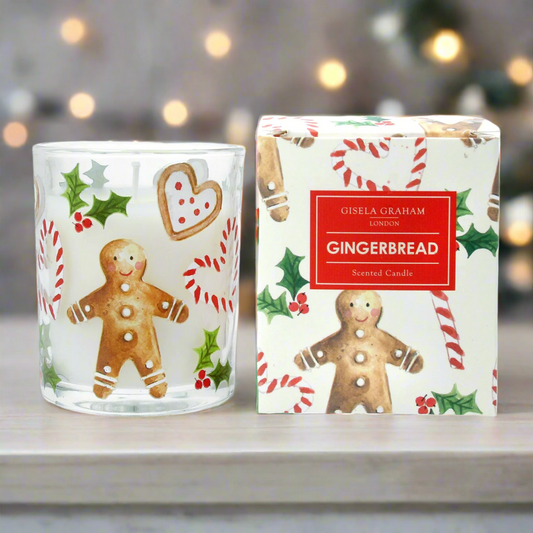 A scented candle with a Christmas gingerbread design, featuring images of gingerbread, candy cane, and holly. The candle is in a glass container, and the packaging has a festive design with 'Gisela Graham' and 'Christmas Gingerbread' text.