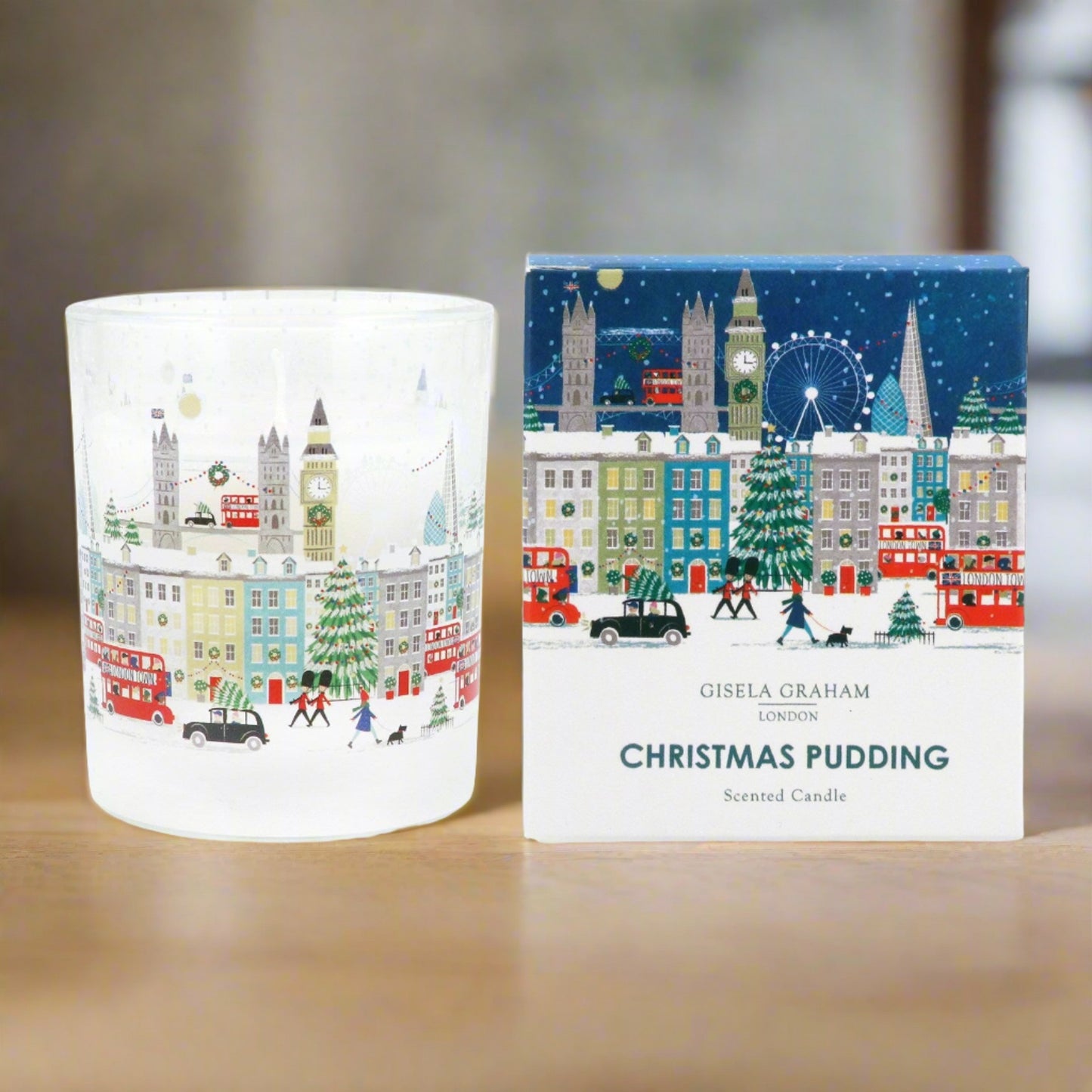 A clear glass scented candle with a Christmas design, featuring an illustration of London landmarks and a Christmas tree, alongside its packaging box with the product title and author's name.