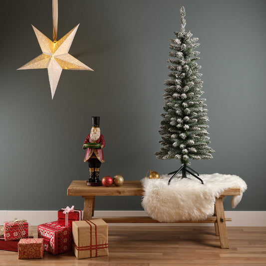 Artificial Christmas tree with snowy pencil pine branches and a classic profile, placed on a wooden bench with presents and a decorative star on a green wall in the background.