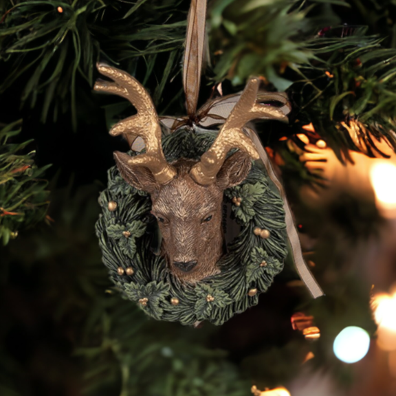 Decorative deer ornament in a wreath hanging on a Christmas tree with blurred lights in the background.