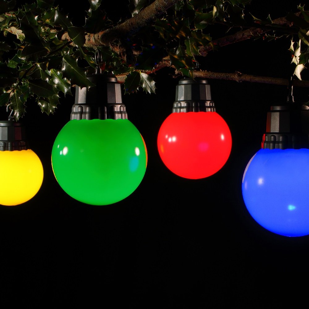 A set of four spherical bulb lights in yellow, green, red, and blue colors hanging outdoors at dusk.