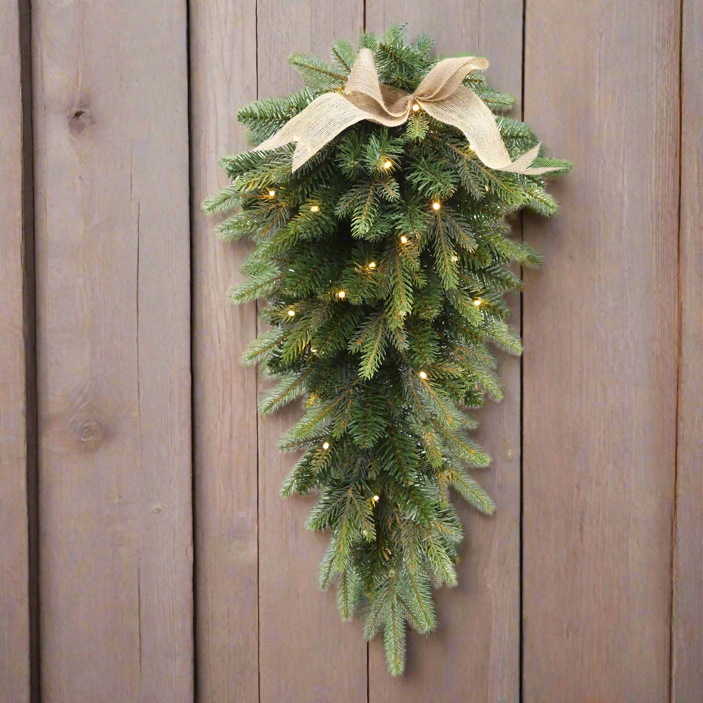 Decorative Christmas swag with lights and a bow on a wooden wall.