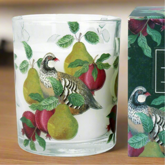 A cylindrical glass candle with a partridge and pear design, sitting next to its packaging box.