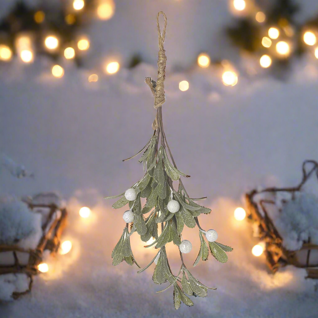 Hanging mistletoe decoration with white berries against a snowy background with lights.