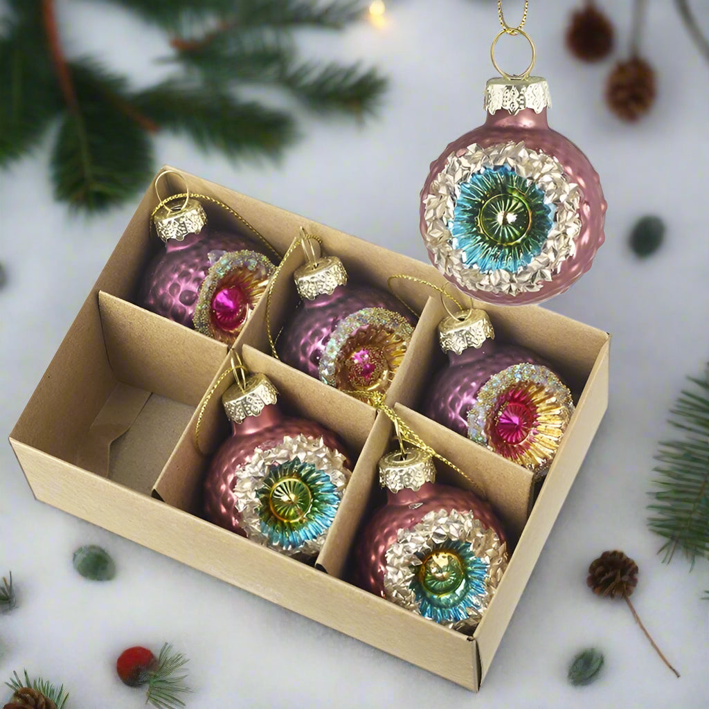 A set of 6 ornate pink glass Christmas baubles displayed in a box, with each bauble featuring a unique design with colors such as pink, blue, and gold.