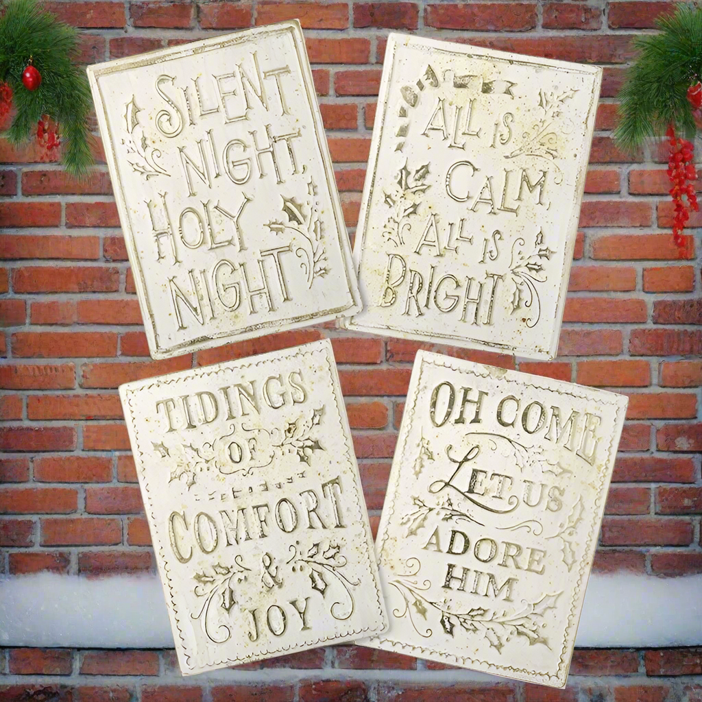 Four Christmas-themed signs with decorative text against a brick wall.
