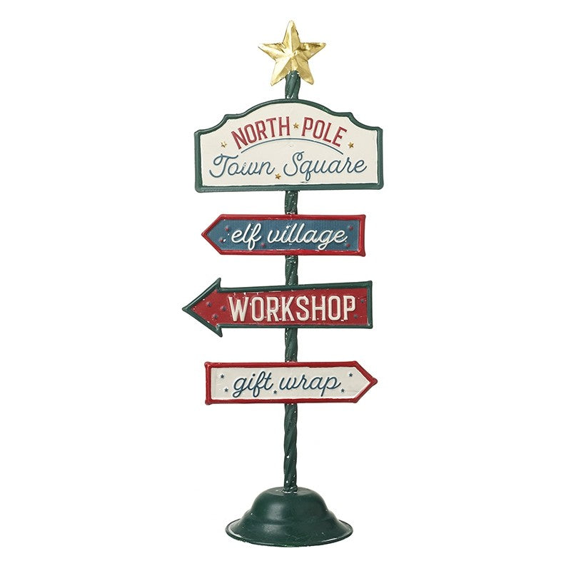 A metal Christmas sign with directional arrows to North Pole Town Square, elf village, and workshop, with a star at the top.