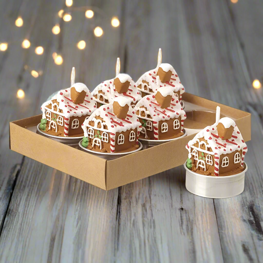 A set of six gingerbread house-shaped tea lights in a cardboard box, with white frosting and red and green candy decorations.