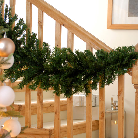 A 270cm green Christmas swag hanging on a wooden staircase with decorative balls and a festive atmosphere.