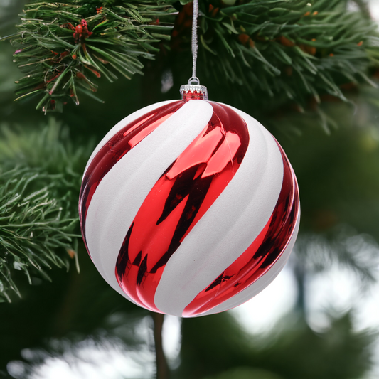 An oversized candy stripe Christmas ornament hanging from a tree, predominantly red and white with a reflective surface.