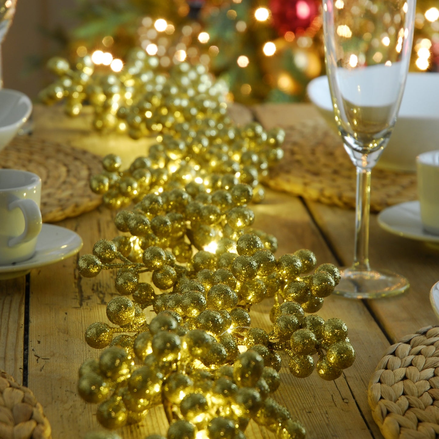 A gold glitter berry lit Christmas garland placed on a table, with a string of lights glowing warm white.