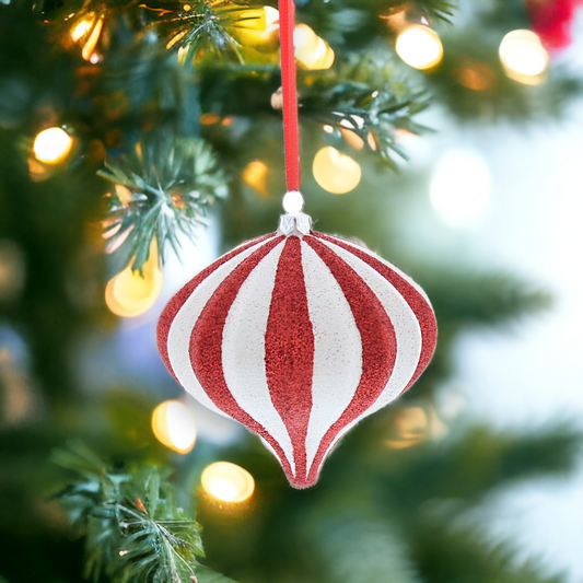 A red and white glittery teardrop-shaped hanging decoration on a Christmas tree with holiday lights.
