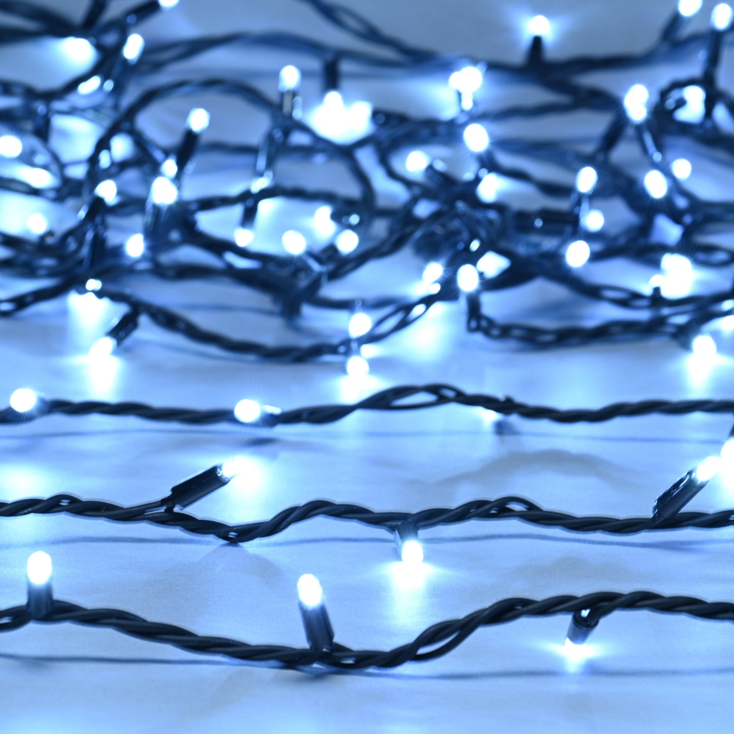 A close-up of connectable white Christmas fairy lights with a black cable and lit bulbs.