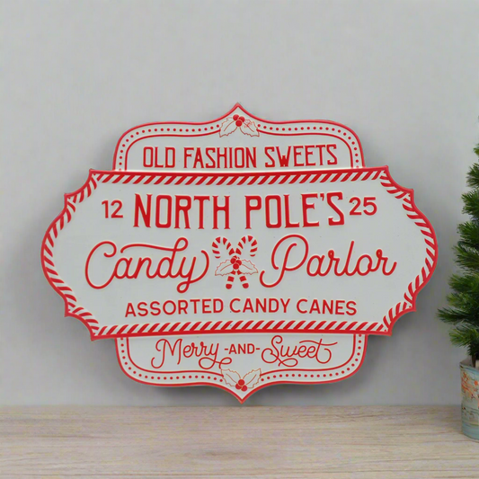 A red and white metal Christmas wall sign that reads 'OLD FASHIONED SWEETS North Pole Parlor Candy Parlor Merry and Sweet' with decorative elements around the text.