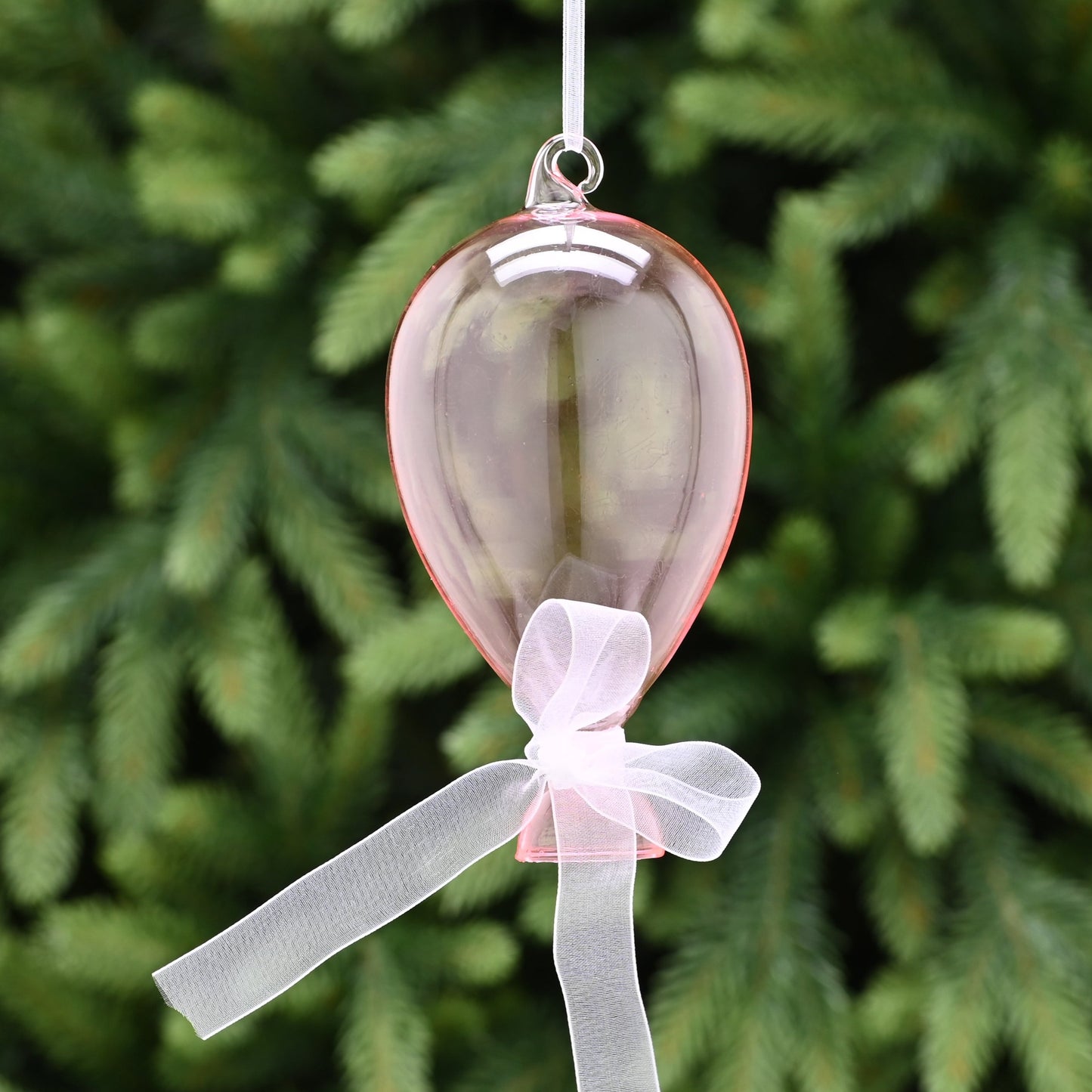 A pink glass balloon with a white ribbon bow, hanging from a tree.