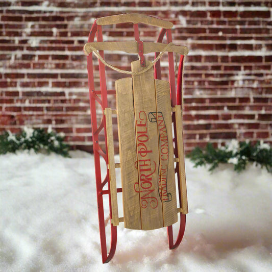 A vintage style sledge display decoration with a red metal frame and a wooden panel adorned with 'NORTHPOLE COMMANDS' and 'LEARN TO FLY' text, designed for Christmas decoration.