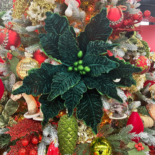 A dark green Christmas poinsettia stem with glitter, placed in a festive Christmas tree with red and gold decorations.