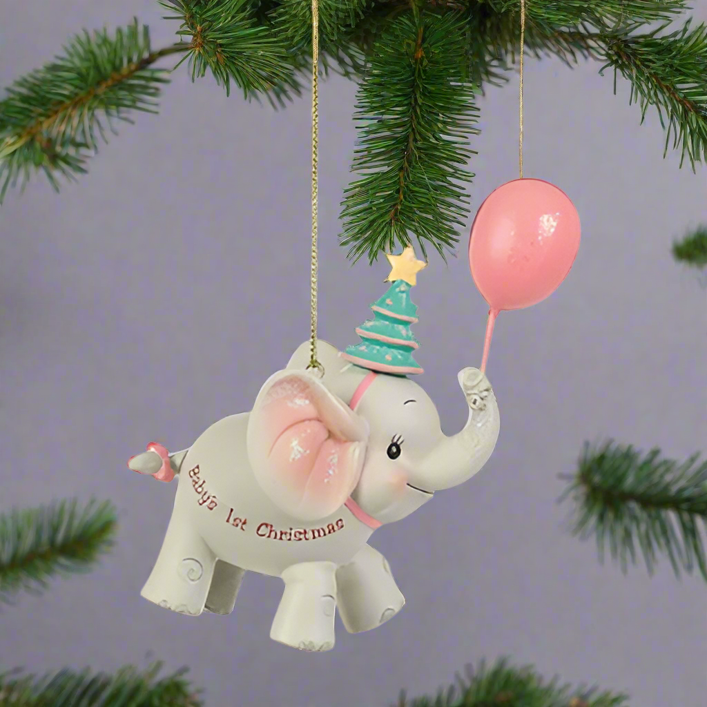 A hanging tree decoration featuring an elephant with a pink balloon and a gold-colored hat, with the text 'Baby's 1st Christmas' on its trunk.