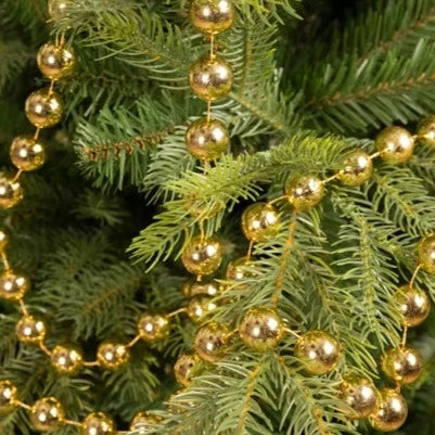 A close-up of a gold bead Christmas garland draped over a green pine tree.