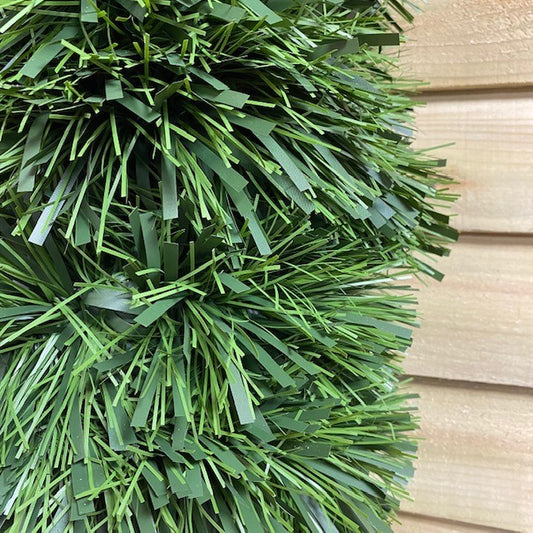 A close-up of a green tinsel Christmas garland with matte finish and a mix of dark and light green foliage.