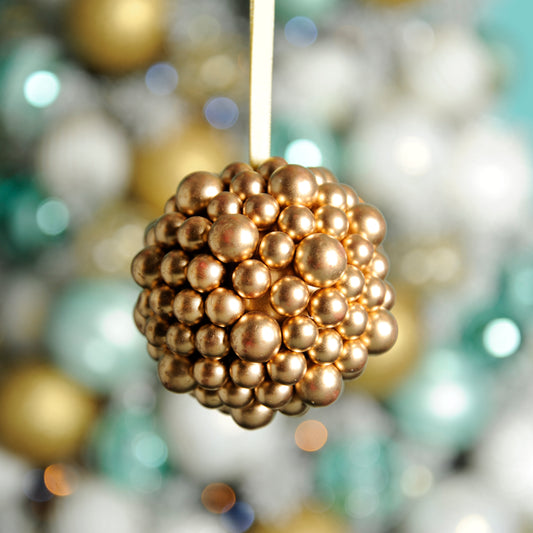 A gold-colored berry cluster ball hanging from a string, surrounded by various Christmas ornaments.