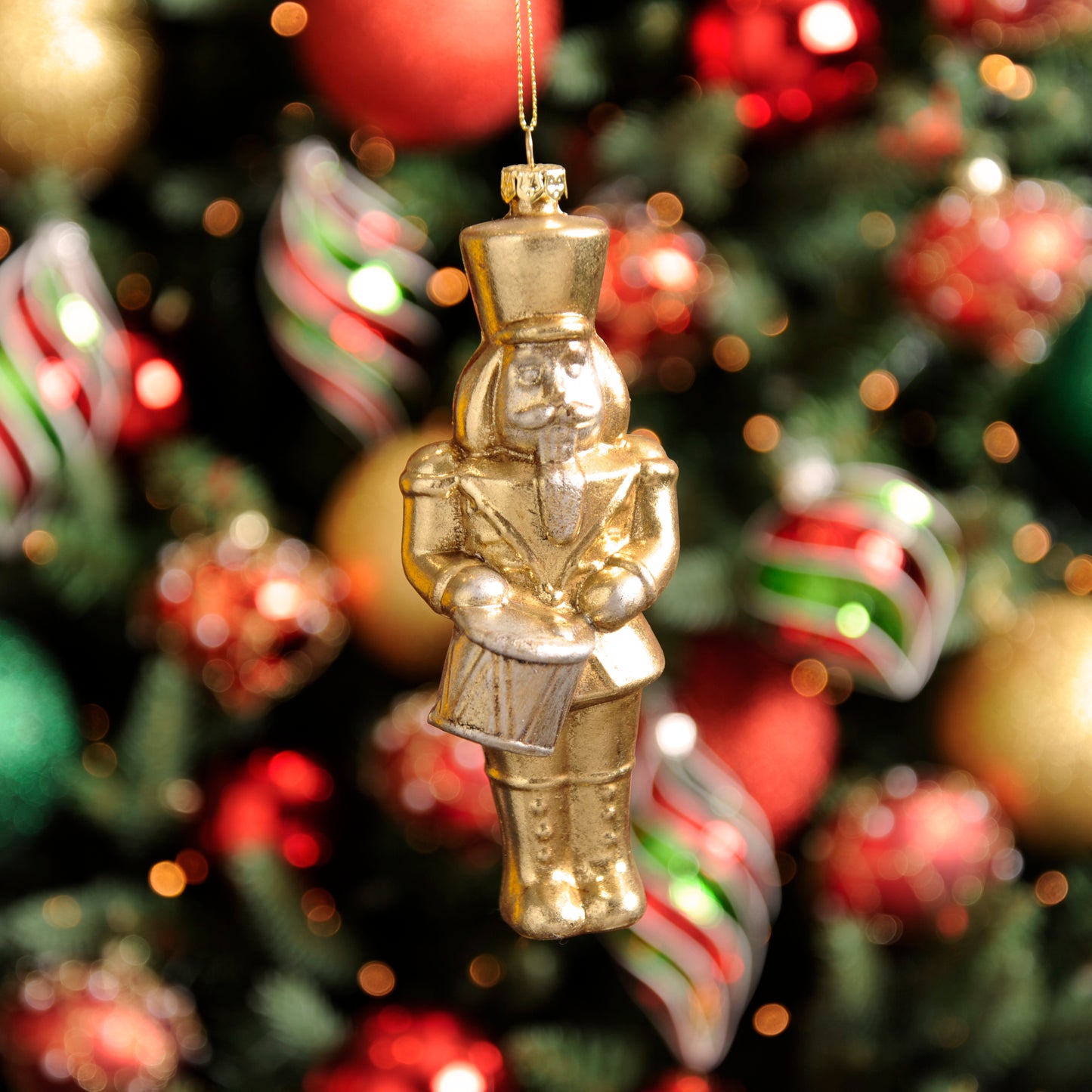 A gold-colored Christmas nutcracker hanging decoration with a uniform, positioned among other holiday decorations on a Christmas tree.