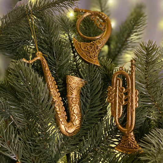 A set of three gold-colored resin Christmas tree decorations shaped like musical instruments, hanging from the branches of a Christmas tree.