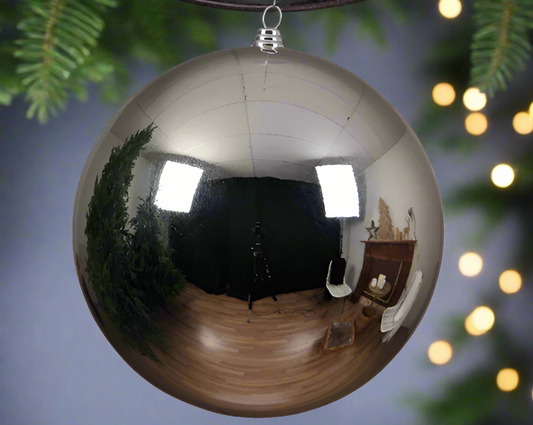 A large silver shiny Christmas bauble hanging from a chain, with a reflective surface, displayed in a room setting.