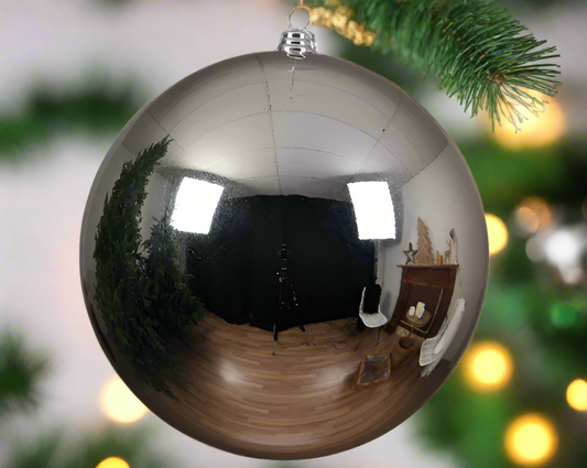 A 25cm silver shiny Christmas bauble hanging from a chain, with a reflective surface showing a blurred image of a Christmas tree and decoration in the background.