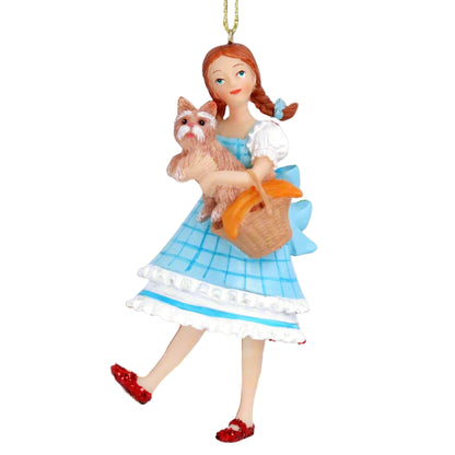 A hanging Christmas tree decoration featuring Dorothy Gale from the Wizard of Oz, holding a basket and wearing a blue and white dress, with a small dog beside her. The decoration is made of resin and has a gold hanging wire.