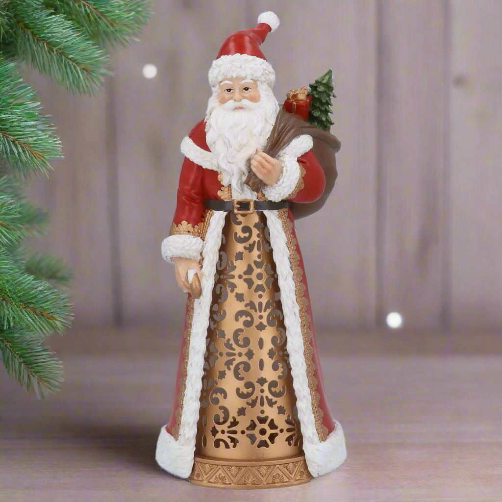 Decorative figure of a traditional Santa Claus holding a bundle of sticks and a small tree on a white background.