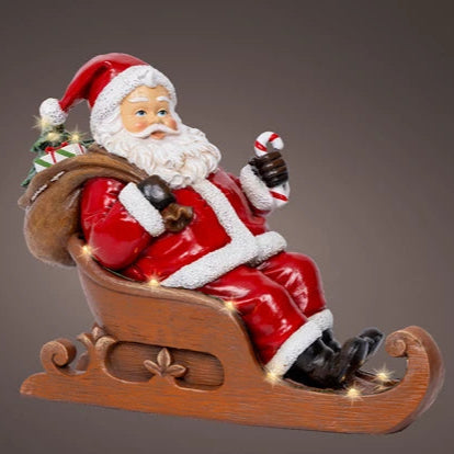 Decorative figure of Santa Claus sitting on a sleigh with a candy cane.