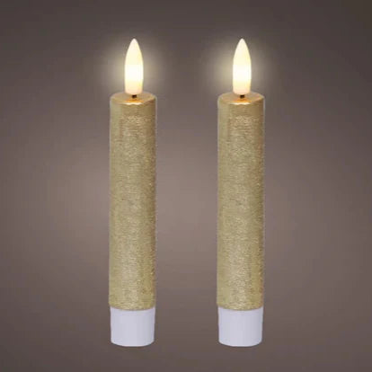 A set of two gold-colored LED wick flat top wax dinner candles with a warm white light, standing on a gray background.