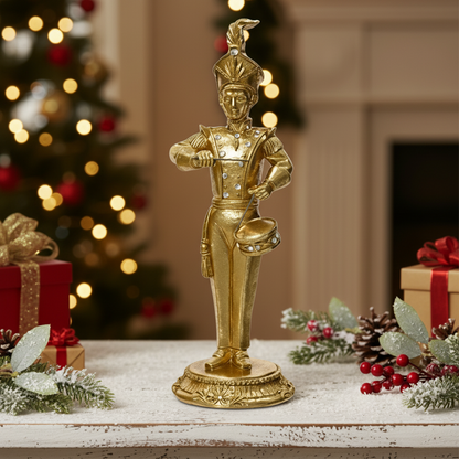 Gold figurine of a drummer in a festive setting with Christmas decorations.
