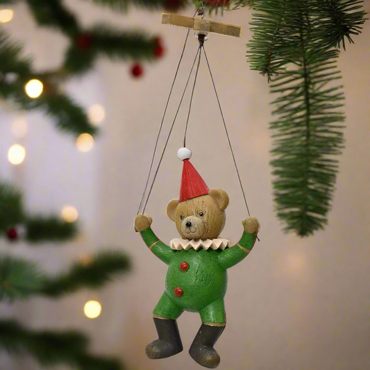 A hanging puppet style teddy bear decoration featuring a brown teddy bear in a green outfit with a red bow, suspended by strings.