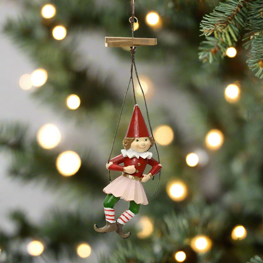 Elf ornament hanging on a Christmas tree with blurred lights in the background