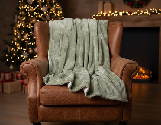 A folded green Christmas tree pattern throw with a sherpa-backed polyester flannel surface.