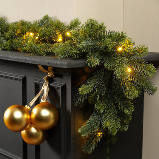Decorative Christmas garland with lights and gold ornaments on a black surface.