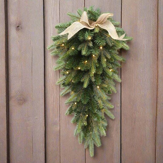 Decorative Christmas swag with lights and a bow on a wooden wall.